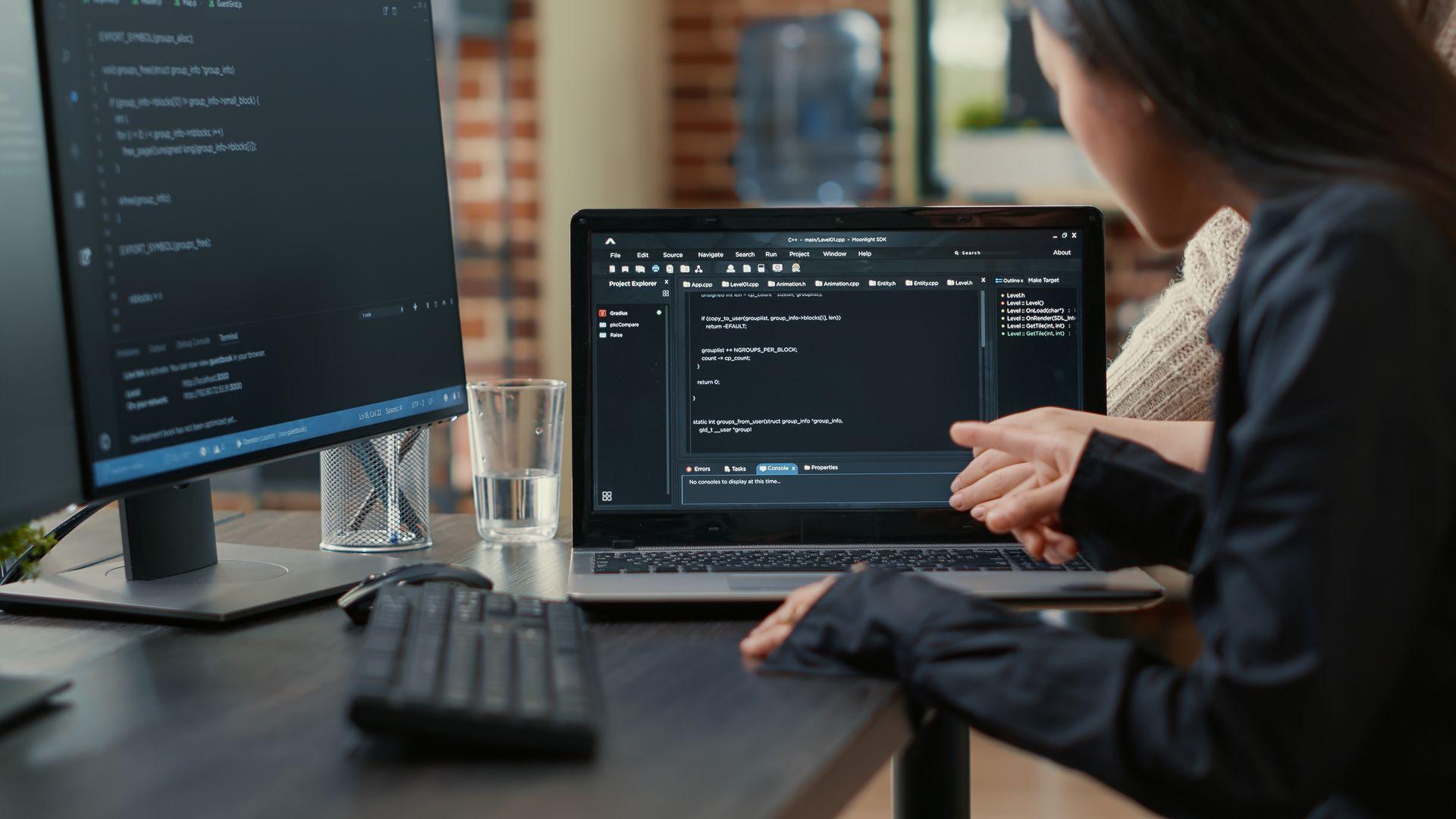 equipo programadores hablando sobre algoritmo que ejecuta pantalla portatil apuntando al codigo fuente mientras sentado escritorio desarrolladores software que colaboran proyecto grupo codificacion da